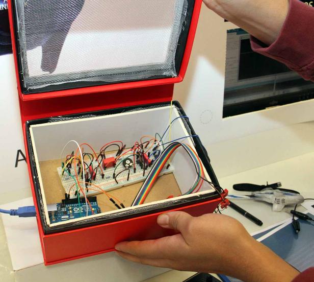 Ein roter Kasten mit geöffnetem Deckel zeigt eine elektronische Schaltung auf einem Steckbrett.