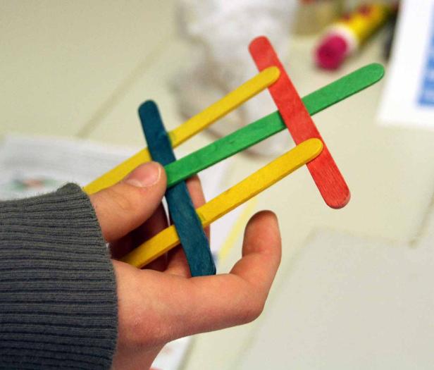 Eine Hand hält ein buntes Gebilde aus Holzstäbchen.