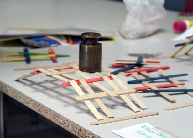 Ein Gewicht steht auf einer kleinen Brücke aus Holzstäbchen.