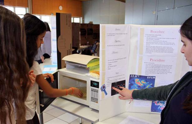 Schülerinnen führen ein Experiment mit einer Mikrowelle und Käse durch.