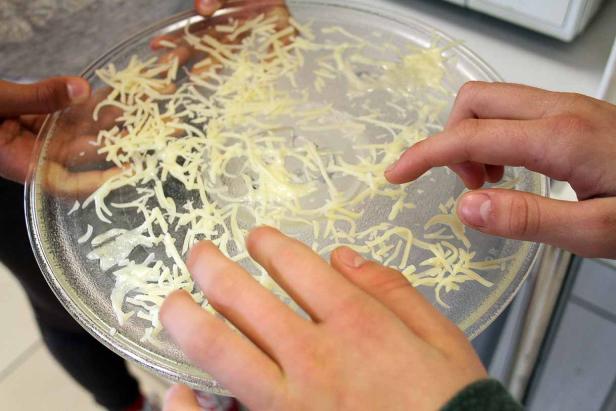 Mehrere Hände berühren geriebenen Käse in einer Glasschale.