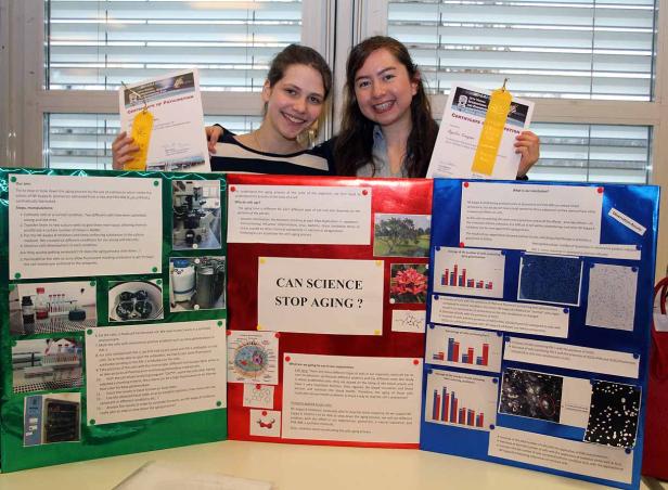 Zwei junge Frauen präsentieren eine wissenschaftliche Ausstellung zum Thema „Kann die Wissenschaft das Altern aufhalten?".