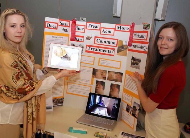 Zwei junge Frauen präsentieren ein Wissenschaftsprojekt über Aknebehandlungen mit Schnecken.