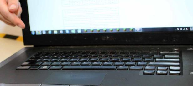 Eine Hand deutet auf den Bildschirm eines schwarzen Laptops.