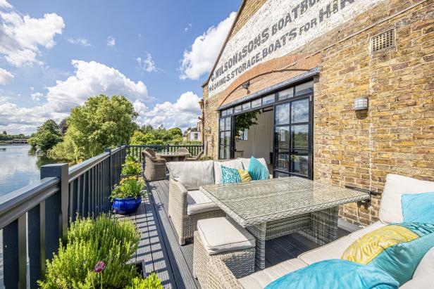 Eine Terrasse mit Korbmöbeln blickt auf einen Fluss an einem sonnigen Tag.