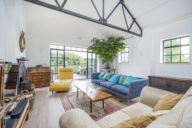 Ein helles Wohnzimmer mit blauen und beigen Sofas, einem gelben Sessel und einer großen Zimmerpflanze.