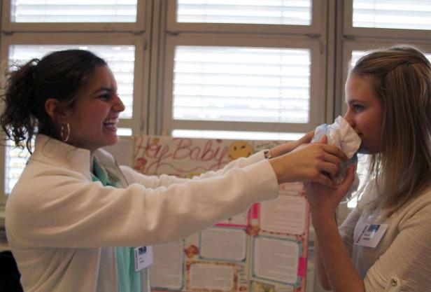 Eine junge Frau hält einer anderen Frau eine Windel vor die Nase.