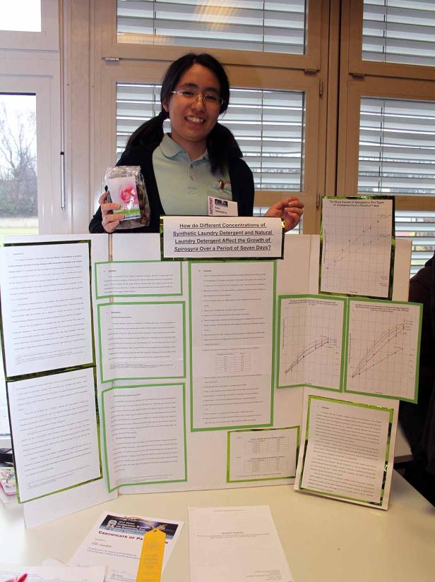 Eine junge Frau präsentiert ein wissenschaftliches Projekt über die Auswirkungen von Waschmittel auf Spirogyra.