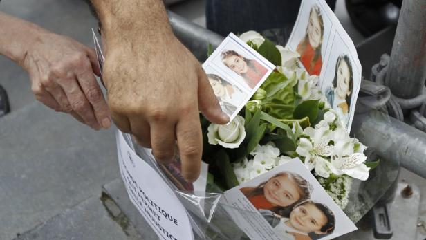 Zwei Hände legen Blumen und Fotos eines jungen Mädchens an einem Gedenkort nieder.