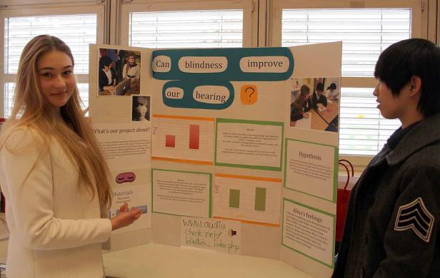 Eine junge Frau präsentiert ein Wissenschaftsprojekt über den Zusammenhang von Blindheit und Gehör.