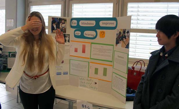 Eine junge Frau hält sich die Augen zu, während ein junger Mann daneben steht und auf eine Präsentation schaut.