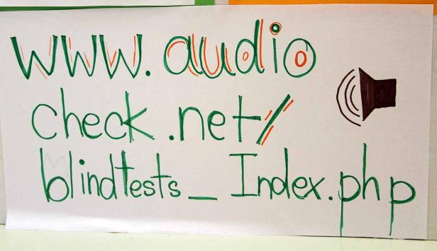 Ein handgeschriebener Zettel zeigt die URL www.audiocheck.net/blindtests_index.php und ein Lautsprechersymbol.