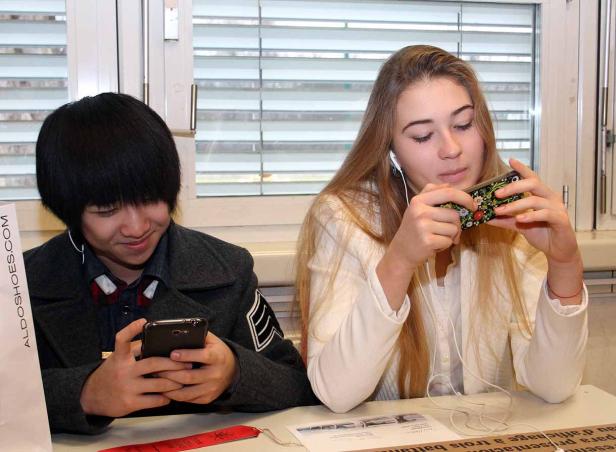 Zwei Jugendliche sitzen an einem Tisch und schauen auf ihre Smartphones.