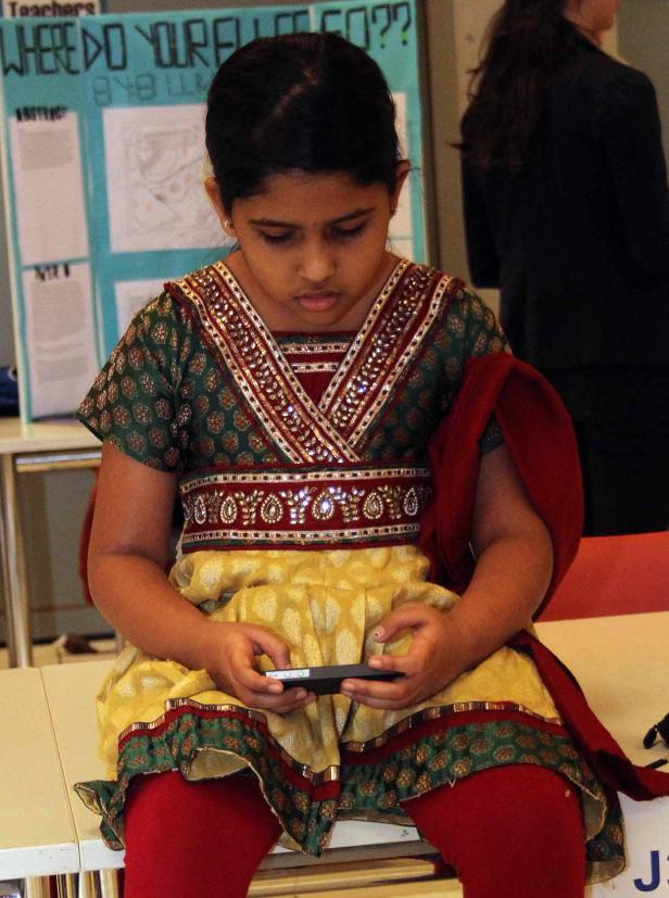 Ein junges Mädchen in traditioneller Kleidung sitzt und benutzt ein Smartphone.