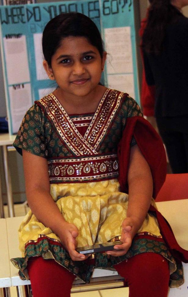 Ein junges Mädchen in traditioneller Kleidung sitzt und hält ein Smartphone.