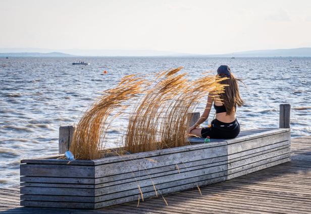Frau sitzt auf einem Holzsteg am Ufer des Neusiedler Sees
