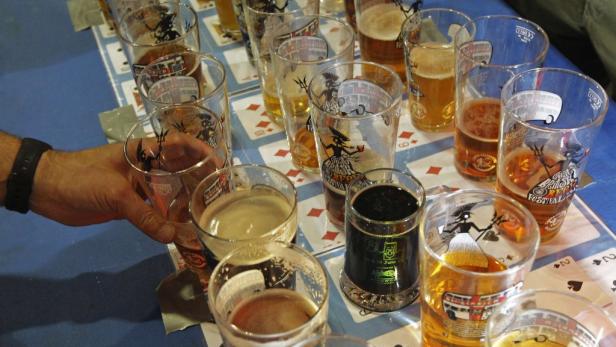 Eine Hand greift nach einem Glas Bier auf einem Tisch mit Spielkartenmuster.