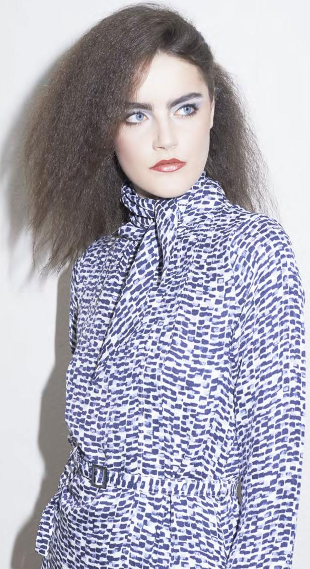 Eine Frau mit blau gemustertem Kleid und auffälligem Haar blickt zur Seite.