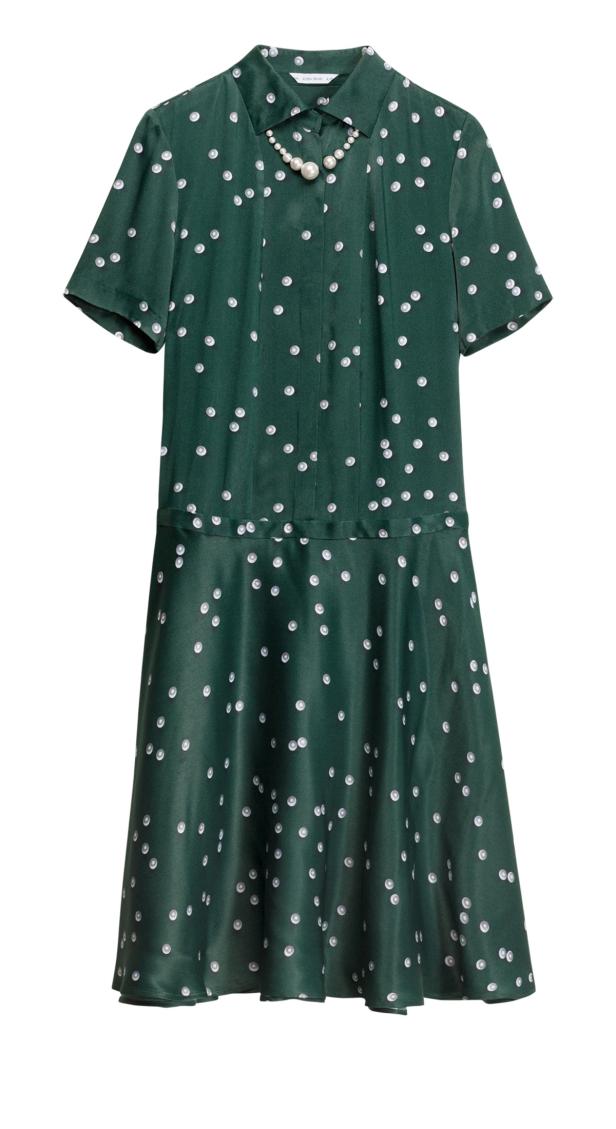 Ein grünes, gepunktetes Kleid mit Kragen und einer Perlenkette liegt vor einem weißen Hintergrund.