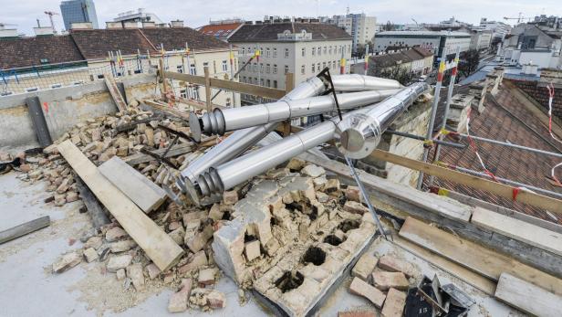 Auf einem Dach liegen Trümmer und silberne Rohre vor einer Stadtkulisse.