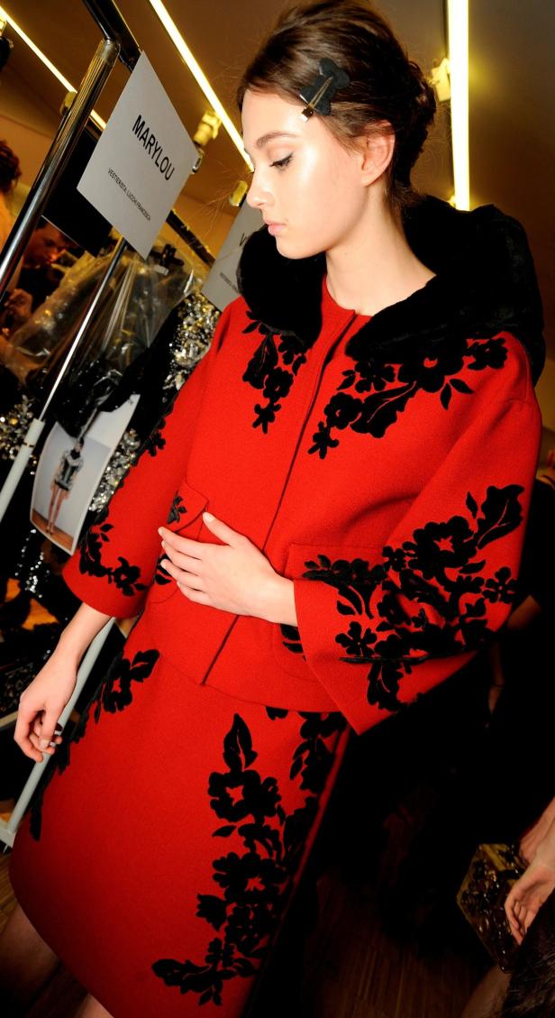 Ein Model trägt ein rotes Kleid mit schwarzen Blumenapplikationen.