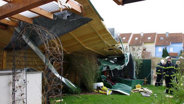 Ein durch ein Unwetter zerstörtes Gartenhaus mit Feuerwehrleuten im Hintergrund.