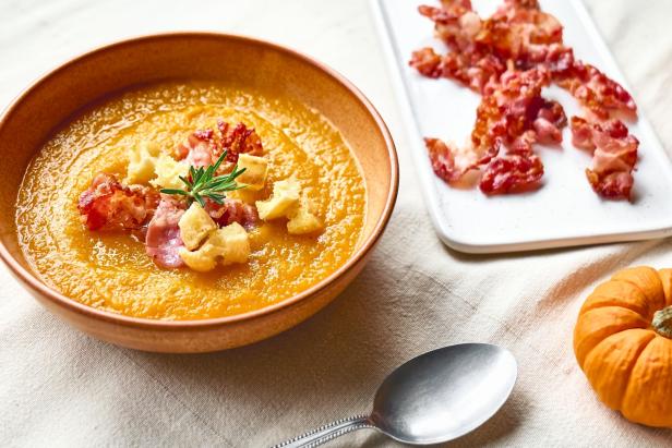 Kürbiscremesuppe mit Speck und Croutons in einem Teller auf einer Leinentischdecke.