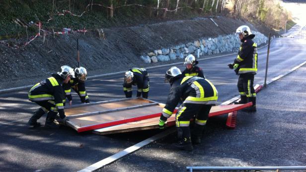 Eine Gruppe Feuerwehrleute hievt eine Holzkonstruktion auf einer Straße.