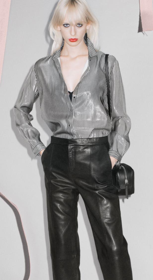 Eine Frau mit blonden Haaren trägt eine gestreifte Bluse und eine schwarze Lederhose mit einer kleinen Handtasche.