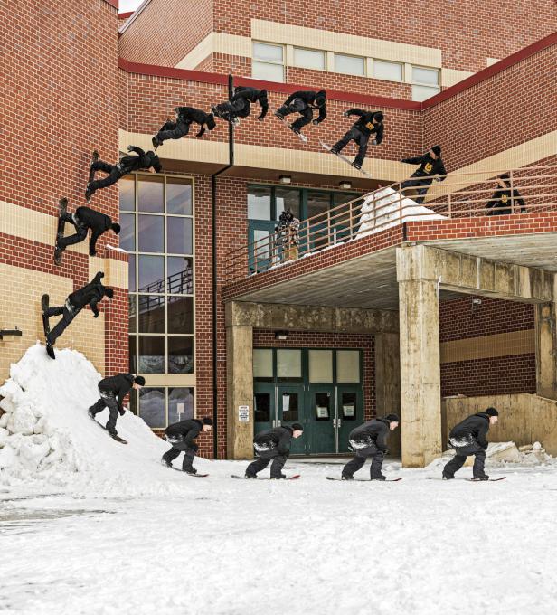 Ein Snowboarder führt vor einem Backsteingebäude eine Reihe von Sprüngen und Tricks aus.