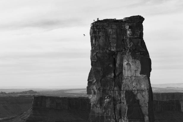 Eine Person springt von einem hohen Felsen, während andere oben stehen.