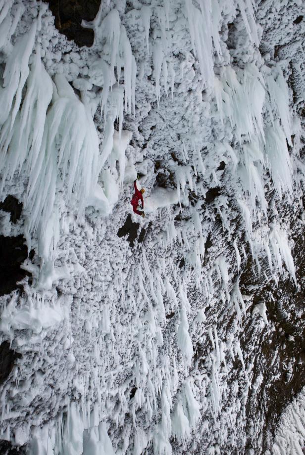Ein Eiskletterer in roter Kleidung erklimmt eine vereiste Felswand.