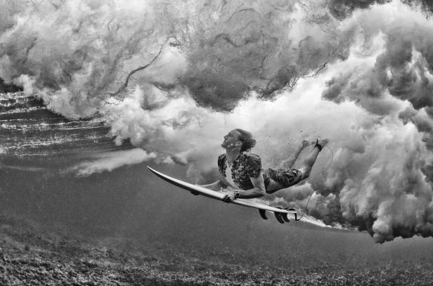 Ein Surfer taucht mit seinem Brett unter einer brechenden Welle hindurch.