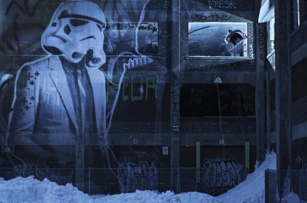 Ein Snowboarder springt durch ein Fenster eines verlassenen Gebäudes mit Graffiti an der Fassade.