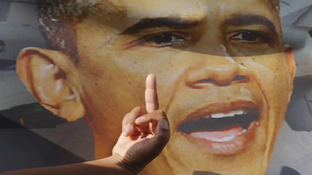 Eine Hand zeigt den Mittelfinger vor einem Porträt von Barack Obama.