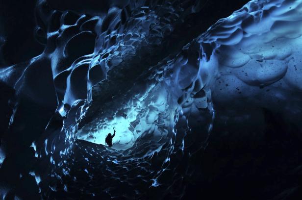Eine Person steht in einer blau beleuchteten Eishöhle.