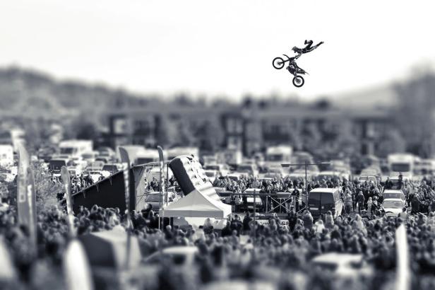 Ein Motocross-Fahrer führt vor einer großen Menschenmenge einen Stunt in der Luft aus.