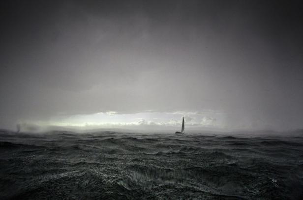 Ein Segelboot kämpft sich durch stürmische See unter einem grauen Himmel.