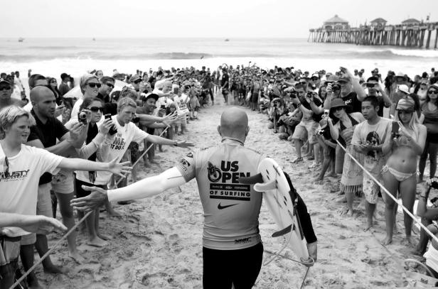 Ein Surfer geht durch eine Menschenmenge am Strand, die ihn fotografiert.