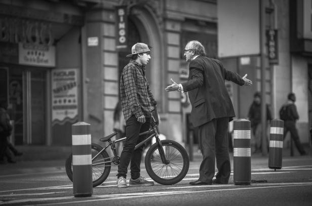 Ein junger Mann mit BMX-Rad diskutiert mit einem älteren Mann im Anzug auf der Straße.