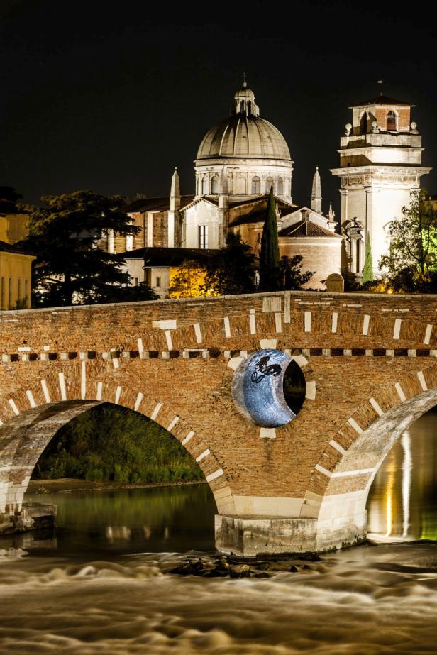 Die beleuchtete Ponte Pietra in Verona bei Nacht mit Blick auf eine Kirche.