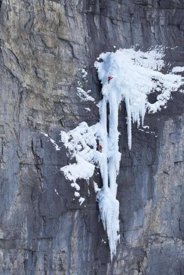 Zwei Eiskletterer erklimmen einen gefrorenen Wasserfall an einer Felswand.