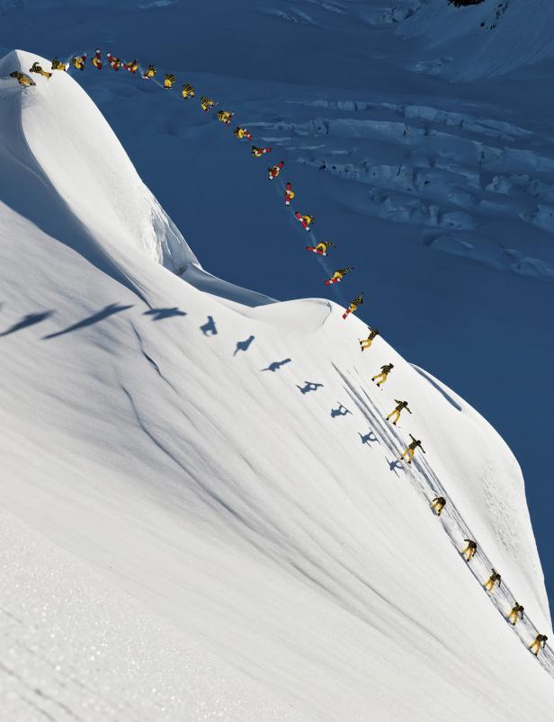 Ein Snowboarder springt und fährt einen steilen, schneebedeckten Hang hinunter.