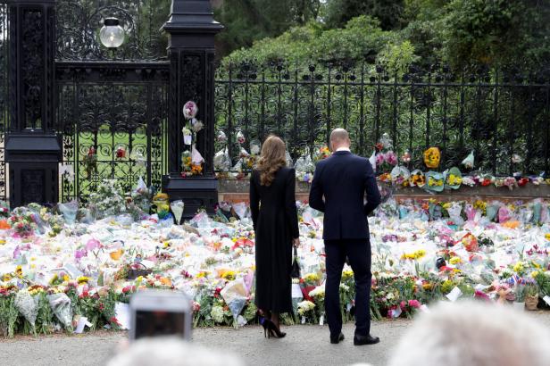 Prinz William und Prinzessin Kate betrachten die Blumengaben vor einem Tor.