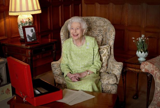 Königin Elizabeth II. sitzt lächelnd in einem Sessel in einem Wohnzimmer.