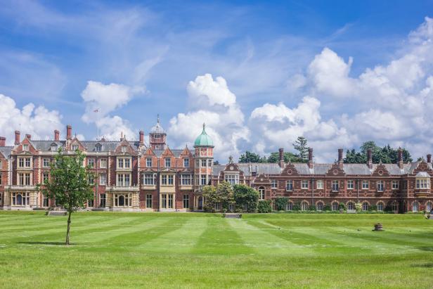 Das Herrenhaus Sandringham House mit weitläufiger Rasenfläche unter blauem Himmel.