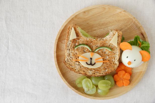 Ein Toastbrot in Katzenform mit Gemüse und ein gekochtes Ei in Form einer Maus auf einem Teller.