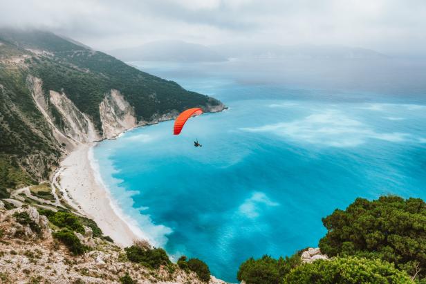 Ein Gleitschirmflieger über dem türkisfarbenen Wasser an einem Strand mit weißem Sand.
