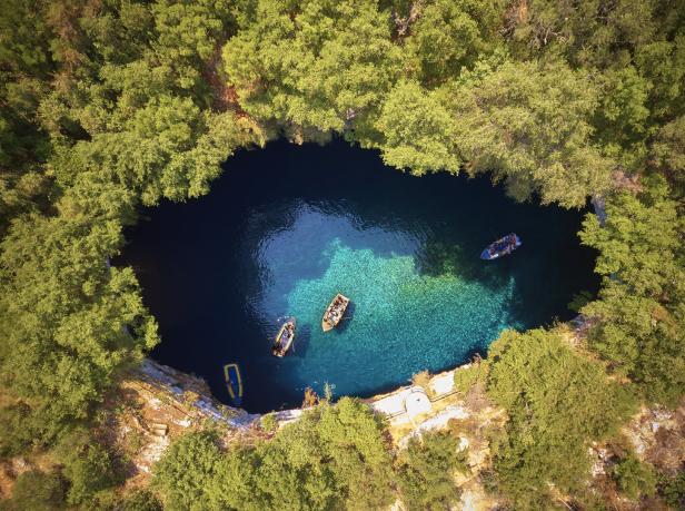 Eine Draufsicht auf den Melissani-See in Griechenland mit kleinen Booten auf dem klaren, türkisfarbenen Wasser.