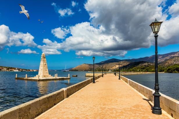Ein langer Pier führt zu einem Denkmal im Wasser, über dem Möwen fliegen.